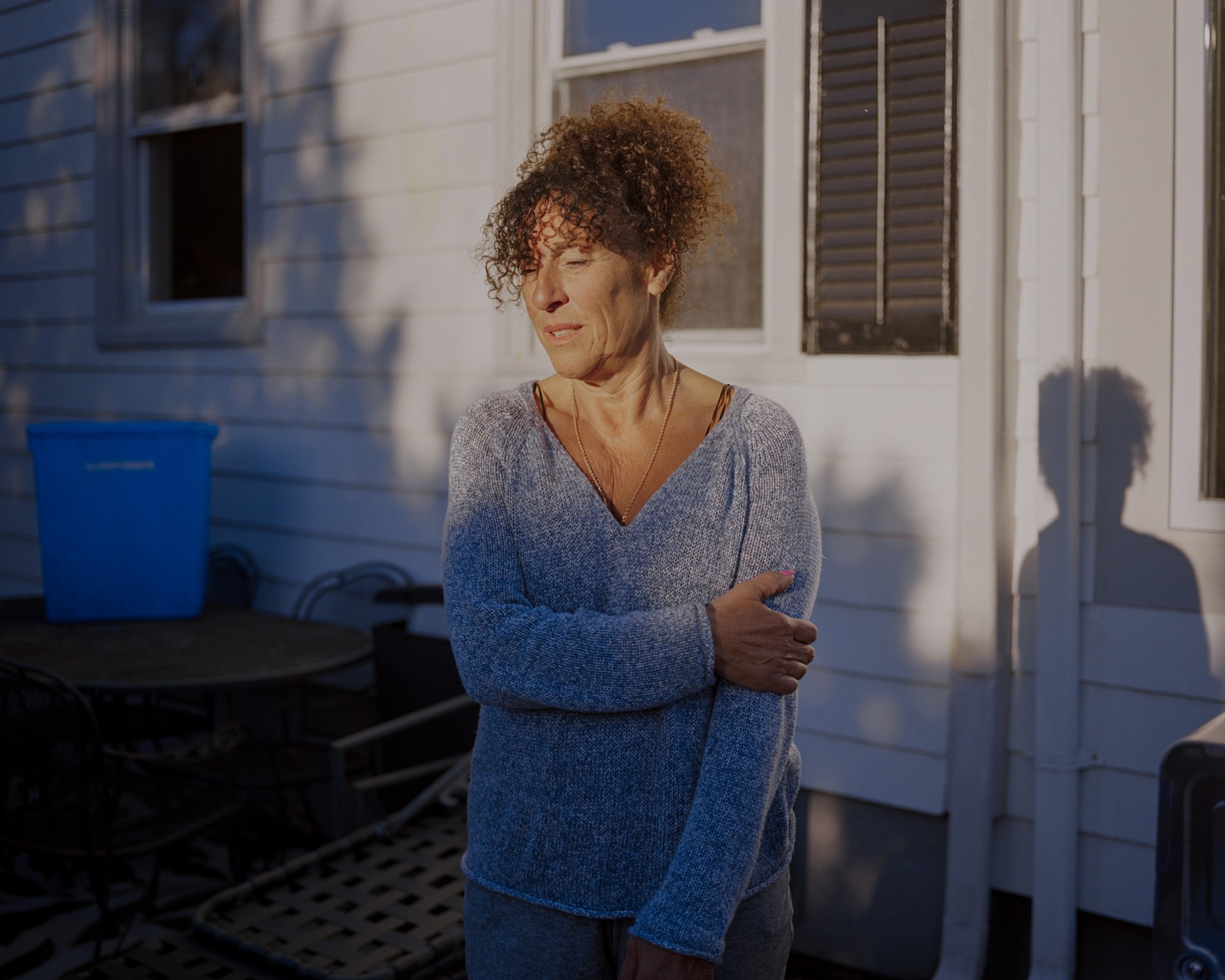 A woman standing in late sunlight beside a house