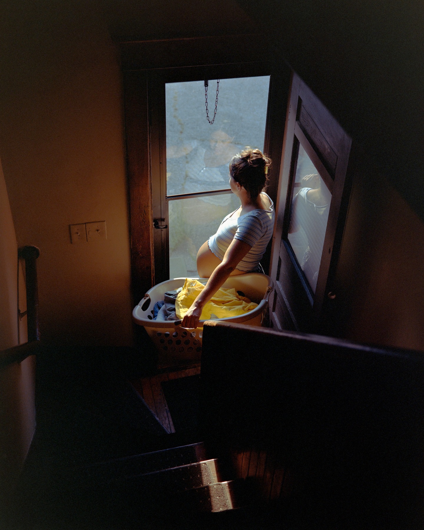 A woman holding a laundry basket in a sunlit doorway