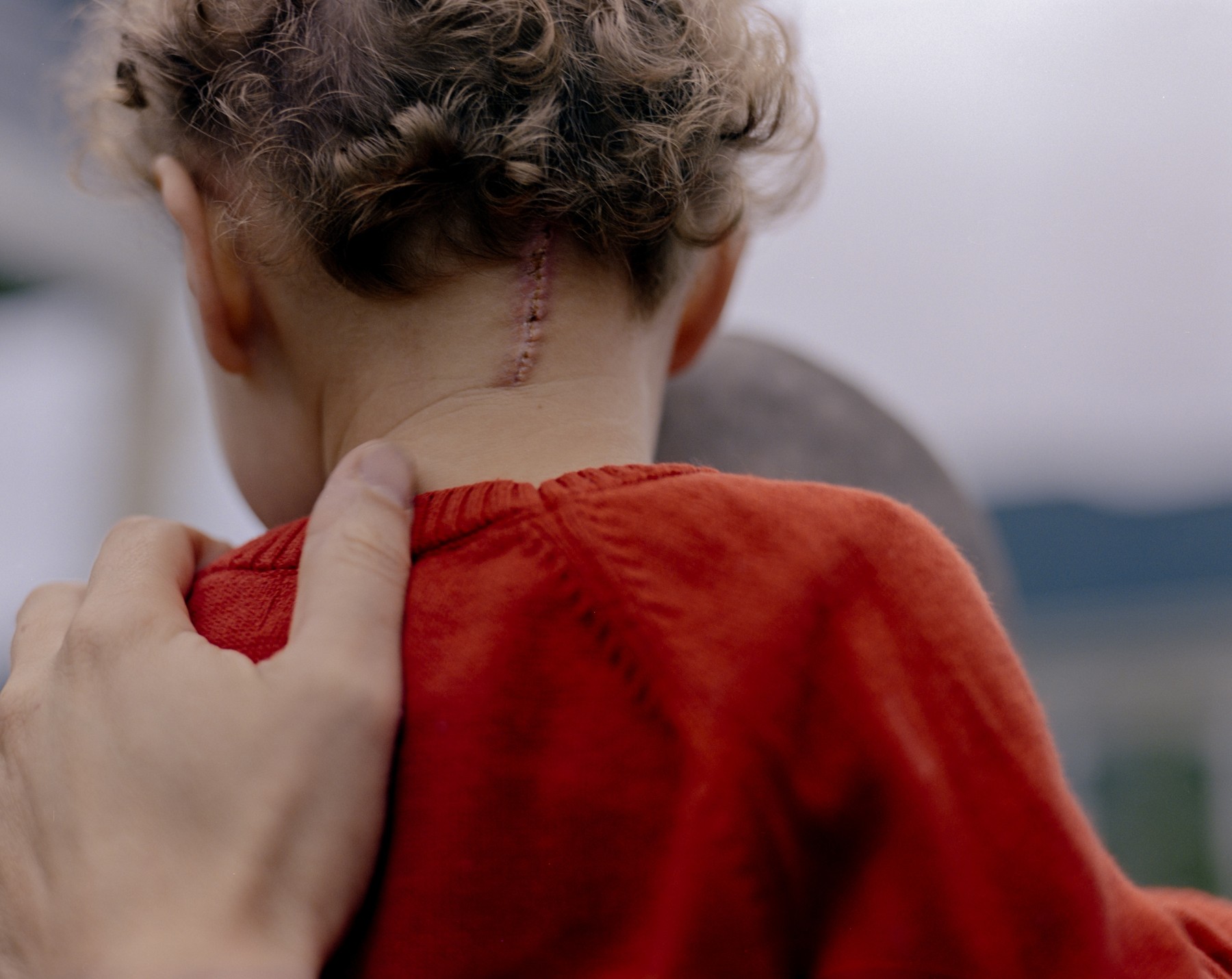 A hand resting against the neck of a child in a red shirt