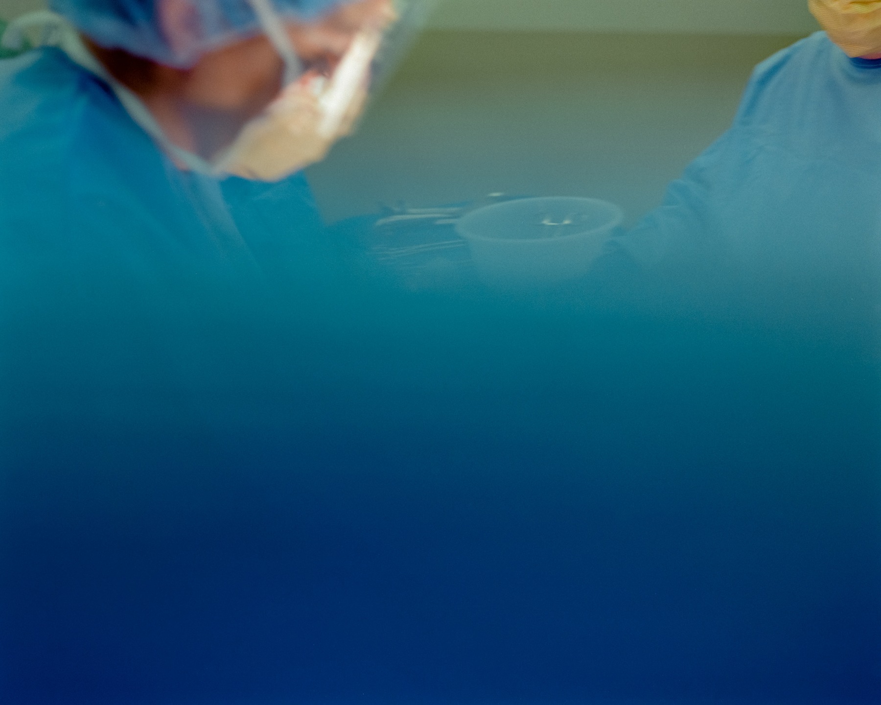 Masked surgical staff behind a blue surgical drape